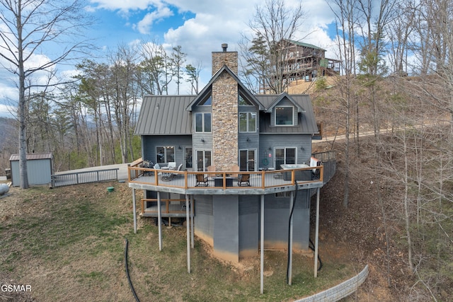 back of house featuring an outbuilding, a chimney, a standing seam roof, metal roof, and a deck