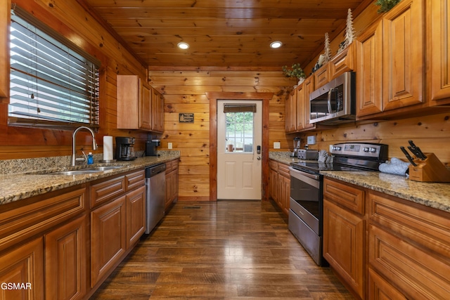 kitchen with wooden walls, light stone countertops, sink, and appliances with stainless steel finishes