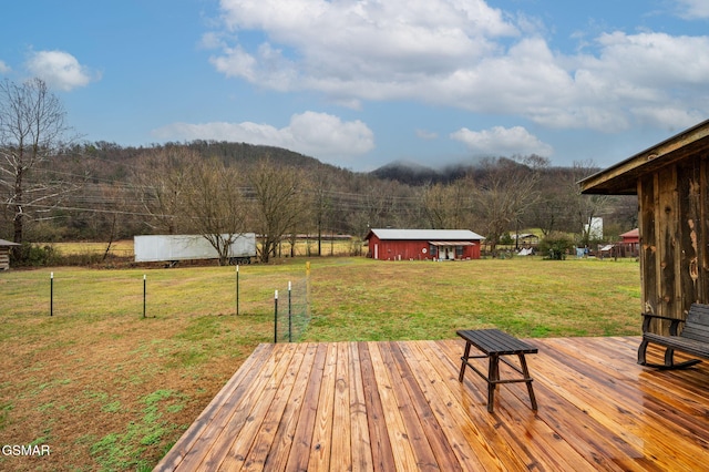 wooden terrace featuring an outdoor structure, a lawn, and fence