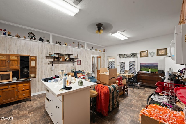 interior space featuring a center island, brown cabinets, ceiling fan, white microwave, and stone finish flooring