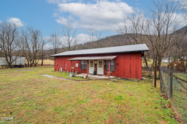 rear view of house featuring fence, a lawn, and metal roof