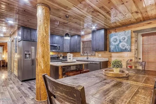 kitchen with wood finished floors, wooden walls, appliances with stainless steel finishes, wooden ceiling, and light stone countertops