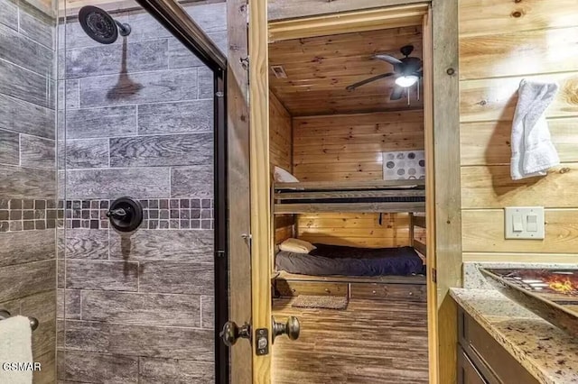 full bath featuring wooden walls, a ceiling fan, and a tile shower