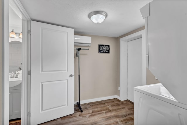 laundry room with a wall mounted AC, light hardwood / wood-style floors, a textured ceiling, and stacked washer and clothes dryer