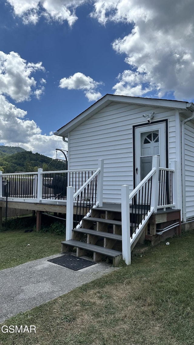 view of exterior entry featuring a lawn and a wooden deck