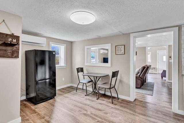 dining room featuring a textured ceiling, light hardwood / wood-style flooring, and a wall mounted air conditioner