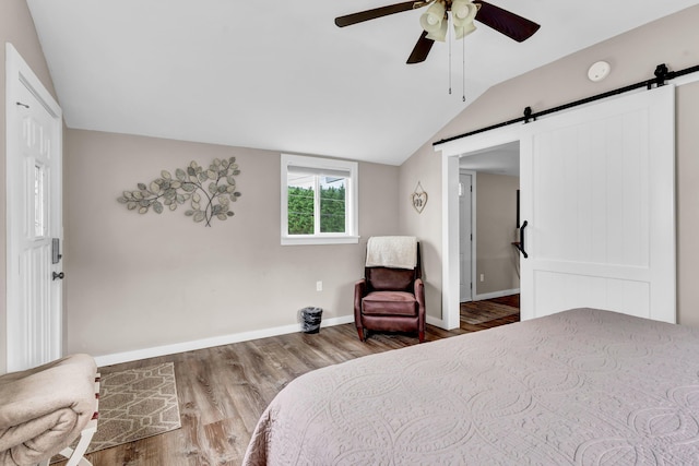 bedroom with a barn door, ceiling fan, wood-type flooring, and lofted ceiling