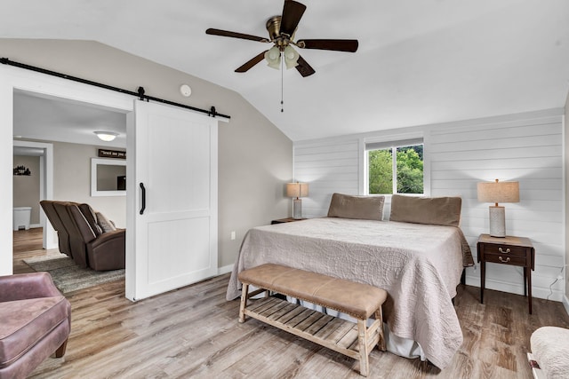 bedroom featuring ceiling fan, a barn door, light hardwood / wood-style floors, and vaulted ceiling