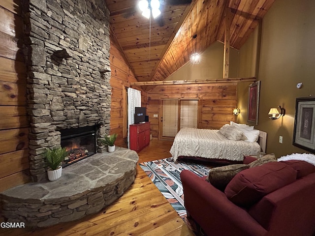 bedroom with high vaulted ceiling, a stone fireplace, wooden ceiling, wood finished floors, and wood walls