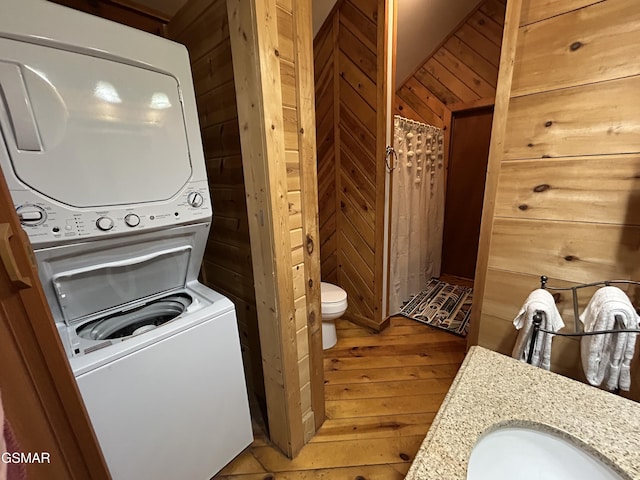 laundry area with light wood-type flooring, wooden walls, stacked washer / dryer, laundry area, and a sink