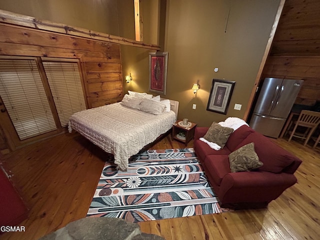 bedroom featuring wooden walls, hardwood / wood-style flooring, and freestanding refrigerator