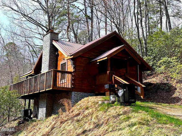 view of front of house featuring a chimney, metal roof, central AC unit, and log exterior