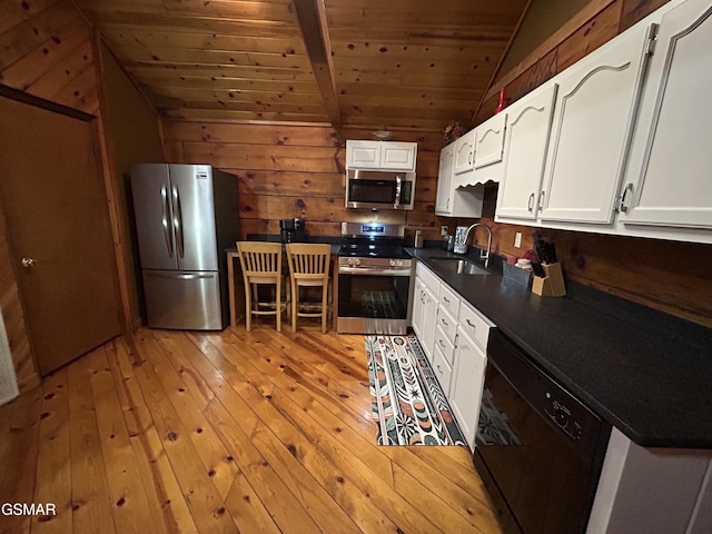 kitchen with appliances with stainless steel finishes, a sink, dark countertops, lofted ceiling, and light wood finished floors