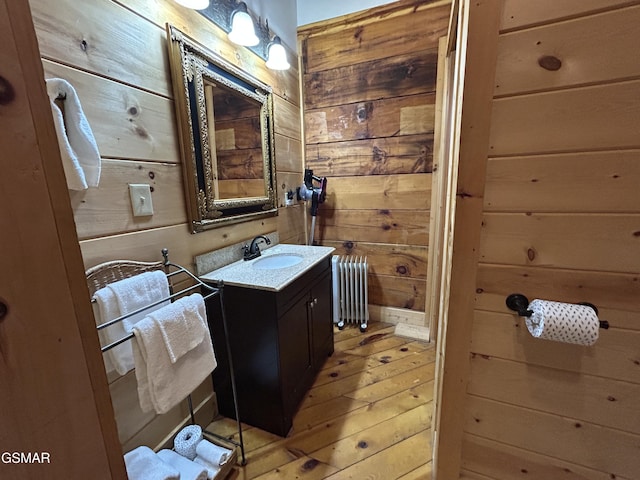 bathroom featuring radiator heating unit, wood walls, vanity, and hardwood / wood-style floors