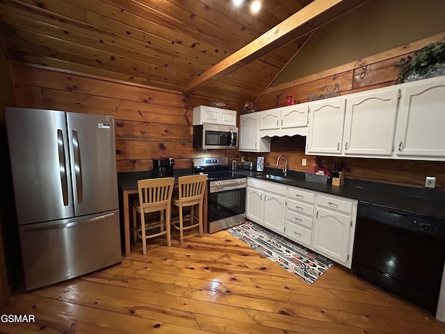 kitchen with appliances with stainless steel finishes, lofted ceiling with beams, white cabinetry, and dark countertops