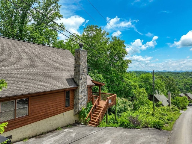 view of side of property featuring stairs, a shingled roof, a chimney, and a wooden deck