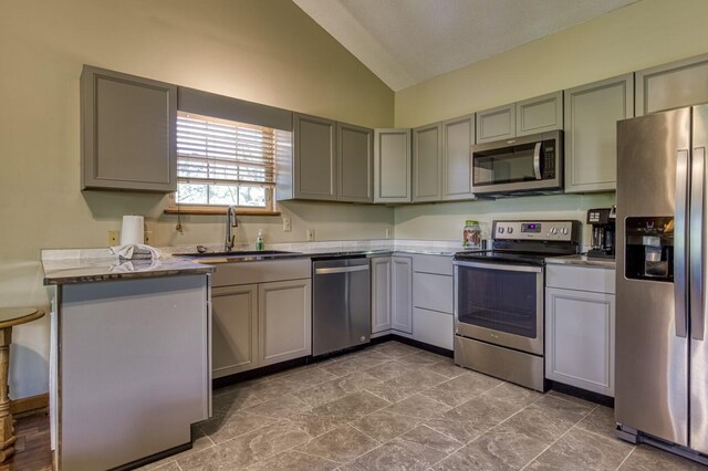 kitchen with kitchen peninsula, stainless steel appliances, vaulted ceiling, sink, and gray cabinets