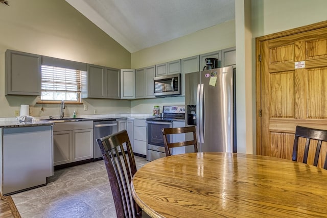 kitchen with gray cabinetry, high vaulted ceiling, sink, appliances with stainless steel finishes, and light stone counters