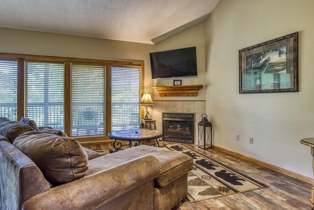 living room with a tile fireplace, a textured ceiling, hardwood / wood-style flooring, and lofted ceiling