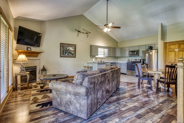 living room featuring dark hardwood / wood-style floors, ceiling fan, high vaulted ceiling, and a tiled fireplace