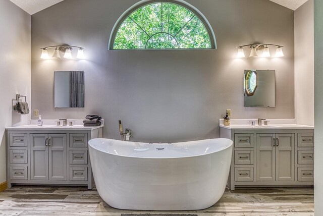 bathroom with a bathtub, wood-type flooring, vanity, and vaulted ceiling