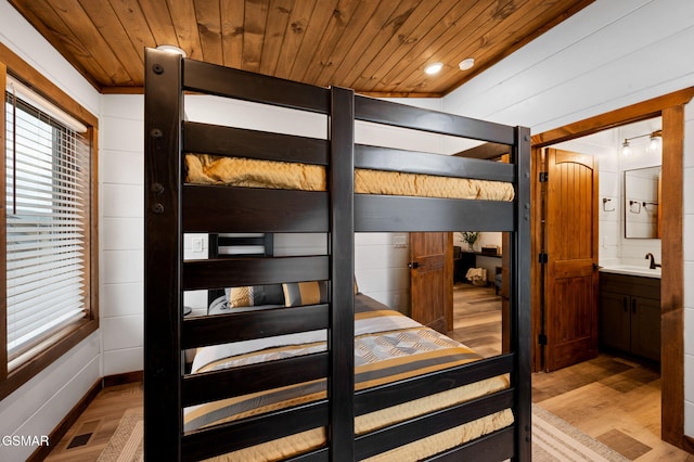 bedroom with ensuite bathroom, light wood-style flooring, a sink, visible vents, and wood ceiling