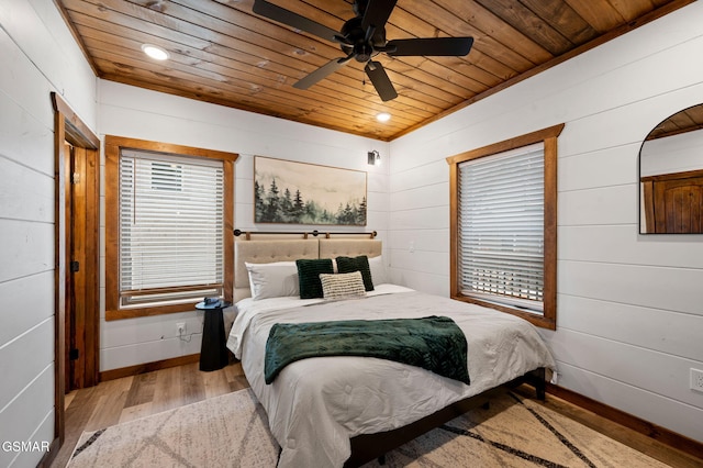 bedroom with wooden walls, wood ceiling, multiple windows, and light wood-style flooring