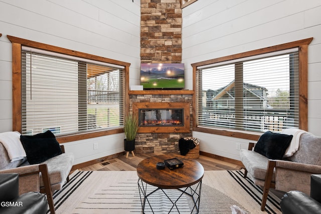 living room featuring wood walls, a fireplace, visible vents, and light wood finished floors