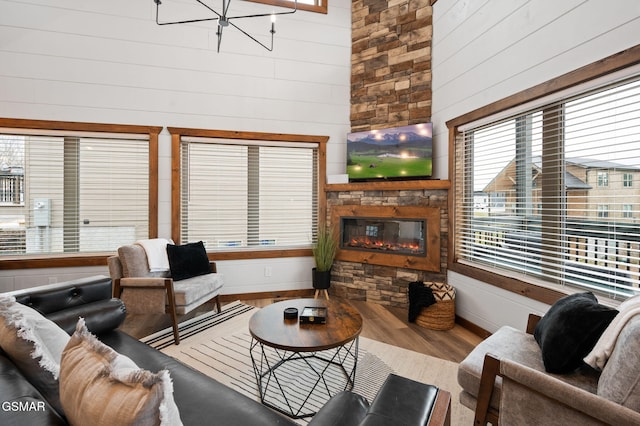 living room featuring wood finished floors, a high ceiling, a stone fireplace, wood walls, and a chandelier