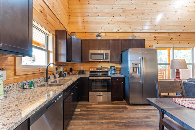 kitchen with wooden walls, light stone counters, sink, and appliances with stainless steel finishes