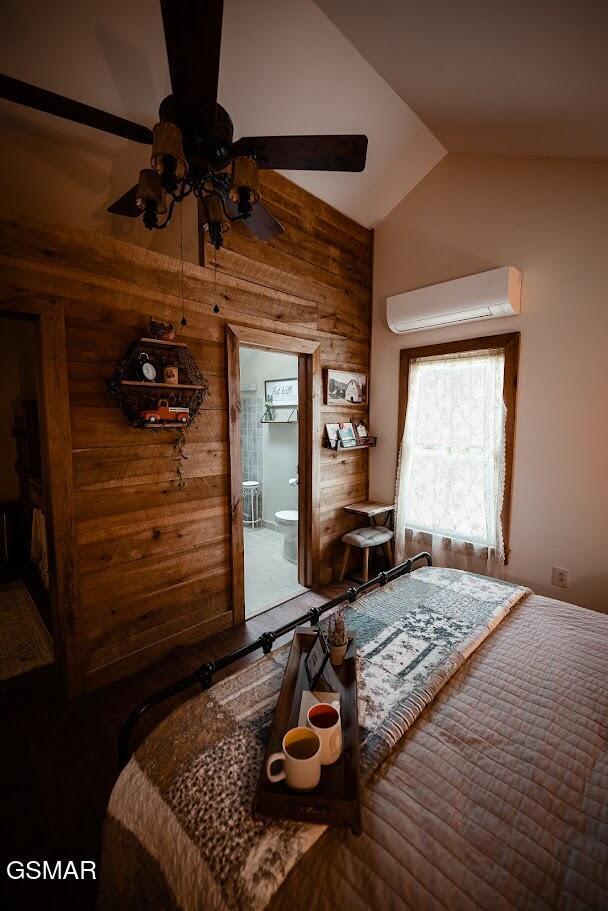 bedroom with ceiling fan, an AC wall unit, wood walls, ensuite bathroom, and lofted ceiling