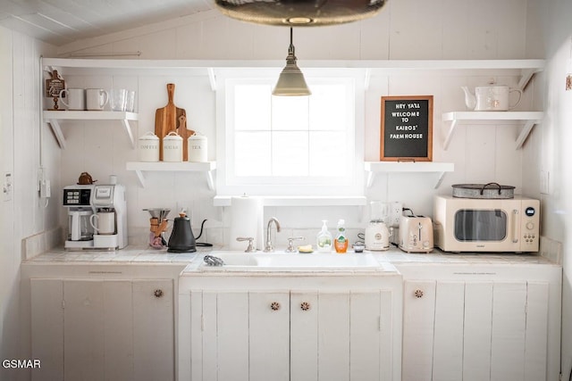 bar featuring white cabinets, decorative light fixtures, sink, and vaulted ceiling