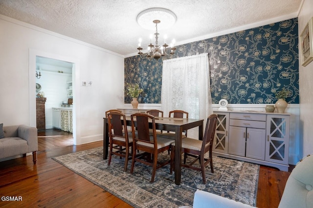 dining room with a chandelier, dark wood-type flooring, a textured ceiling, and ornamental molding