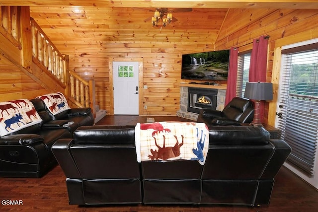 living area featuring lofted ceiling, stairway, wooden walls, wood finished floors, and a lit fireplace