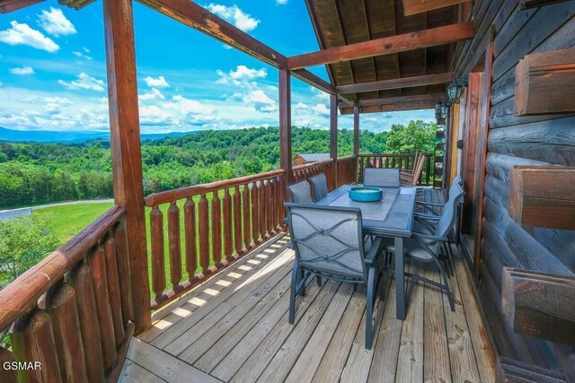 wooden terrace featuring outdoor dining space and a wooded view