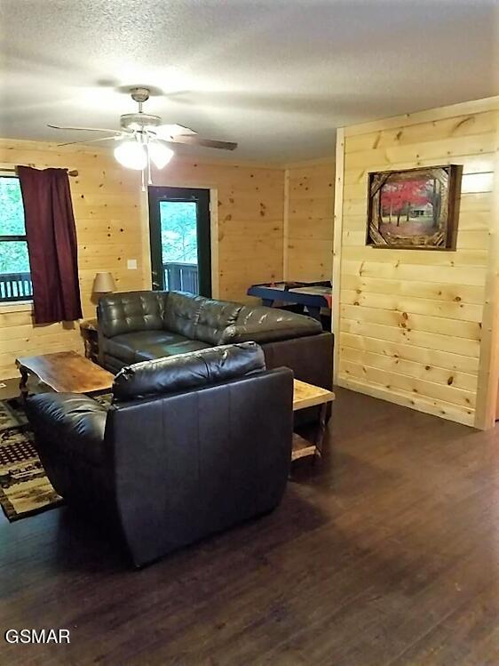 living room with wood walls, ceiling fan, and dark wood-type flooring