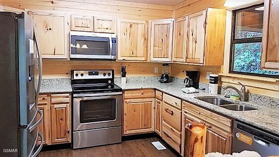 kitchen featuring dark hardwood / wood-style flooring, light stone counters, stainless steel appliances, sink, and wood walls