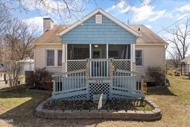 rear view of property featuring covered porch, a lawn, a chimney, and a shingled roof