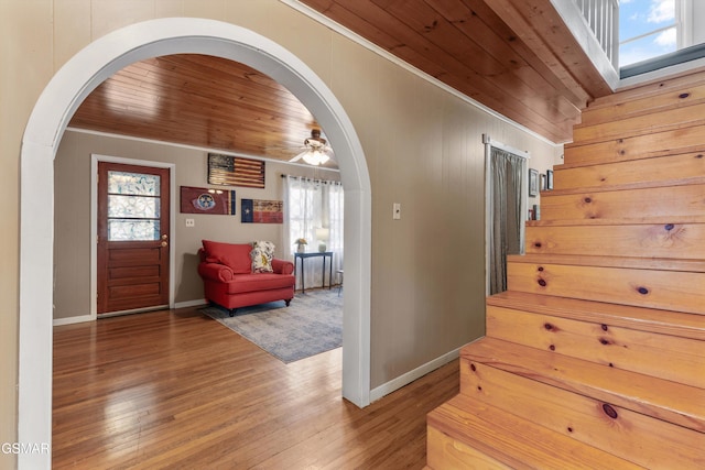 interior space featuring ornamental molding, wood finished floors, arched walkways, baseboards, and wood ceiling