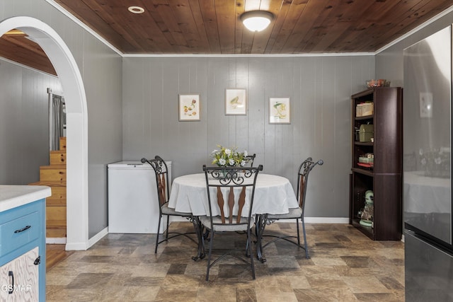 dining area featuring baseboards, arched walkways, and wooden ceiling