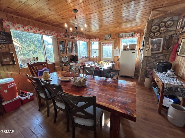 dining space with dark hardwood / wood-style flooring, wooden walls, and an inviting chandelier