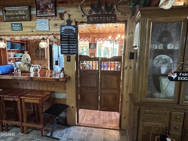 bar featuring wood walls, stainless steel fridge with ice dispenser, and an inviting chandelier