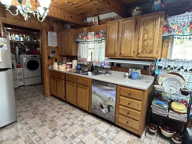 kitchen featuring washer and clothes dryer, wood walls, an inviting chandelier, sink, and appliances with stainless steel finishes