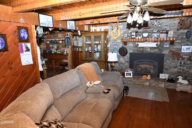 living room with ceiling fan, wooden walls, beam ceiling, wooden ceiling, and a stone fireplace