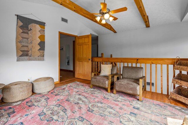 living area with ceiling fan, lofted ceiling with beams, a textured ceiling, and light wood-type flooring