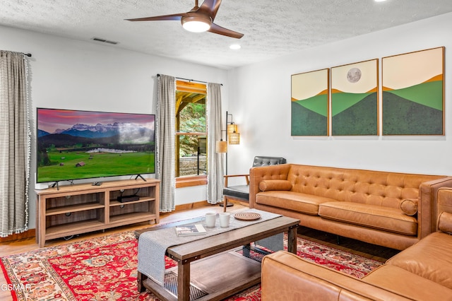 living room with hardwood / wood-style flooring, ceiling fan, and a textured ceiling