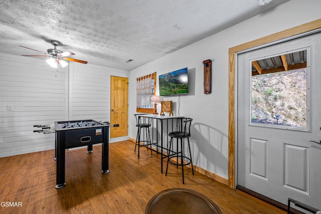 game room featuring hardwood / wood-style floors, a textured ceiling, ceiling fan, and wood walls