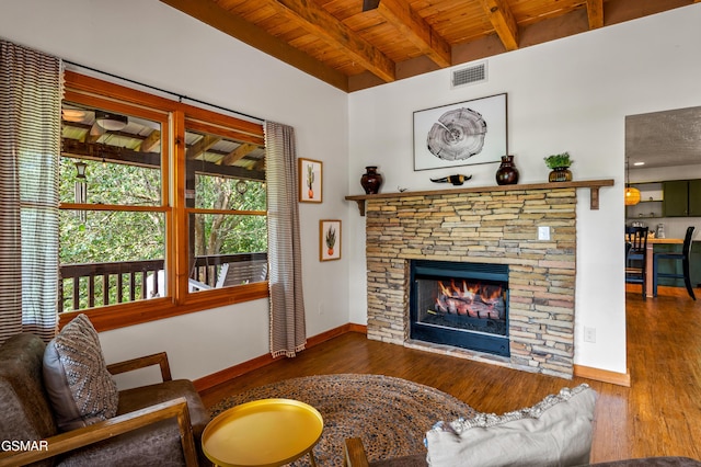 living room with beamed ceiling, a stone fireplace, wood ceiling, and dark wood-type flooring