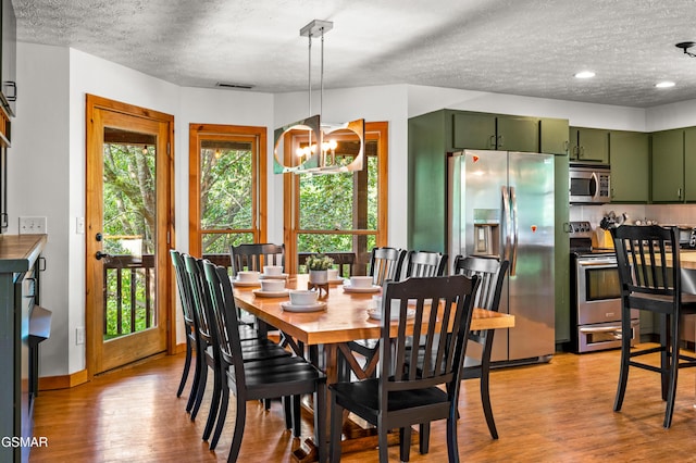 dining area with a textured ceiling, light wood-type flooring, and a notable chandelier