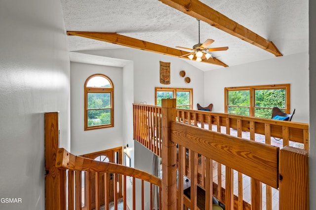 stairway with a textured ceiling, lofted ceiling with beams, and ceiling fan